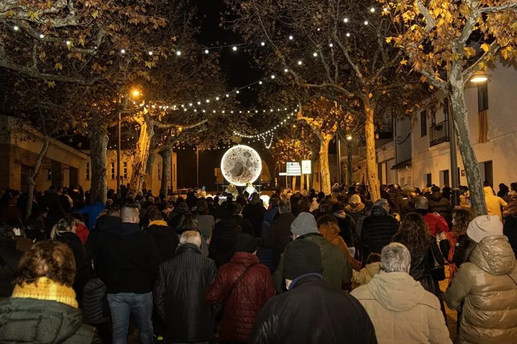 Imatge on s'hi pot veure molta gent escoltant als Reis mags parlant amb una llum amb forma de lluna de fons.